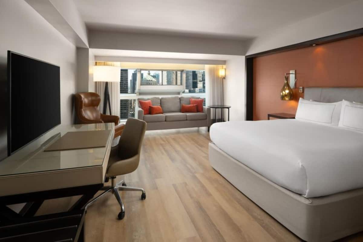 Une chambre d’hôtel moderne dotée d’un grand lit, d’un bureau, d’une chaise, d’une télévision et d’un canapé avec vue sur la ville.