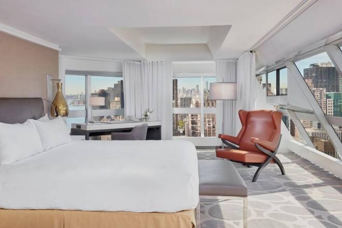 Une chambre d’hôtel équipée d’un lit, d’un bureau, d’une chaise et d’une grande fenêtre donnant sur la ville.