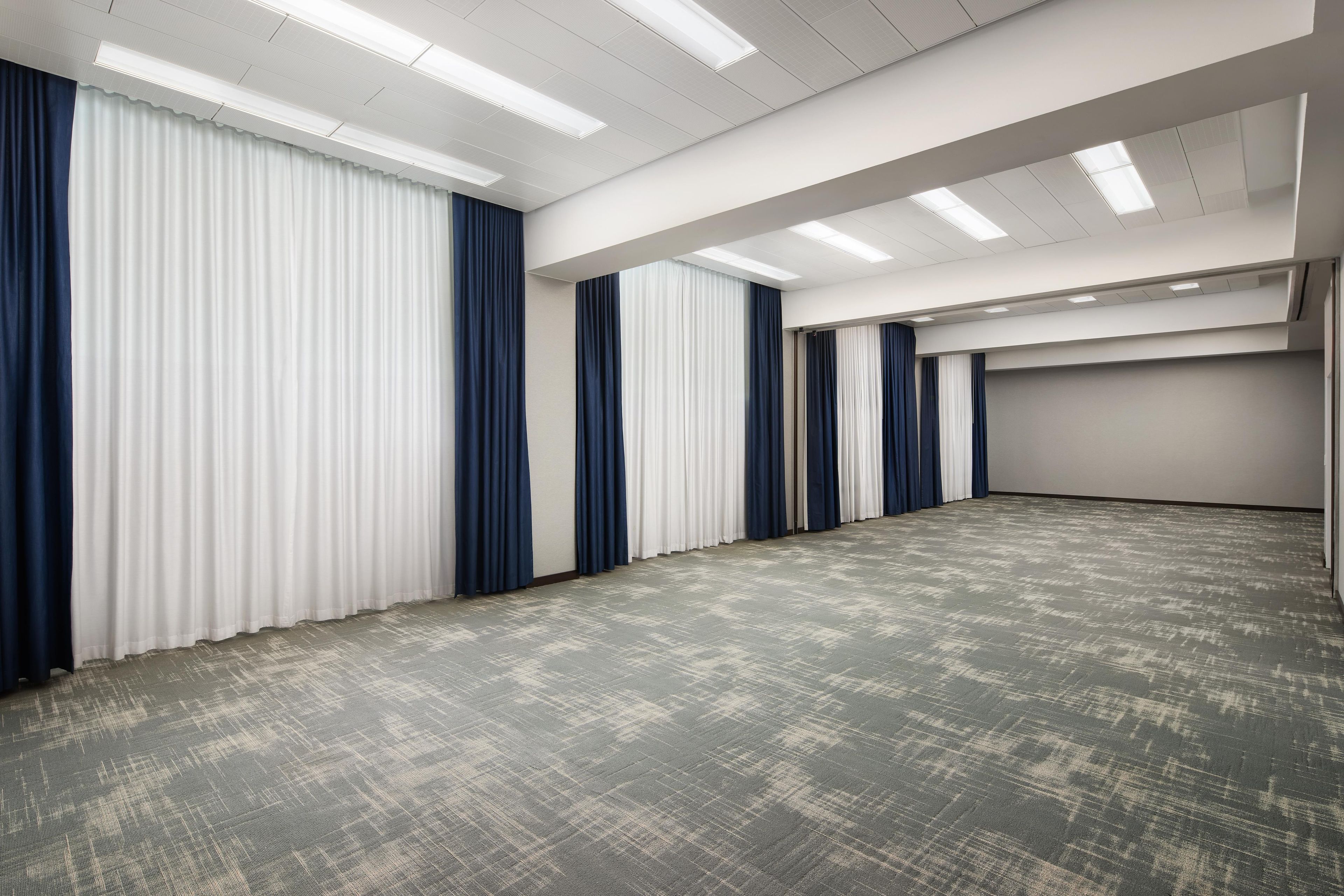 Un amplio salón de conferencias con alfombra estampada, paredes blancas y una fila de cortinas.