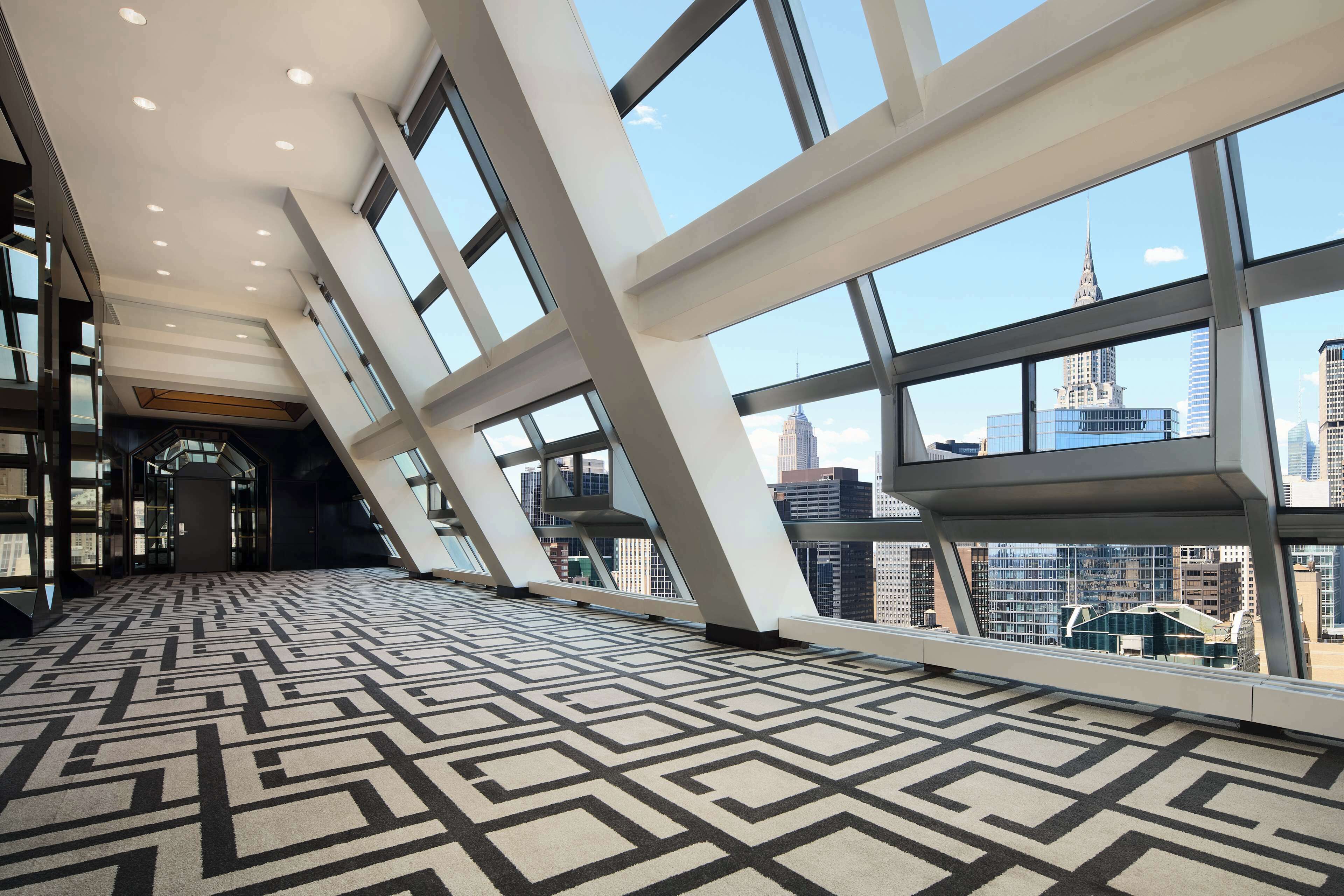 Un hall d’entrée spacieux, doté d’un sol orné de motifs géométriques, de grandes fenêtres offrant une vue sur la ville et d’une architecture moderne.