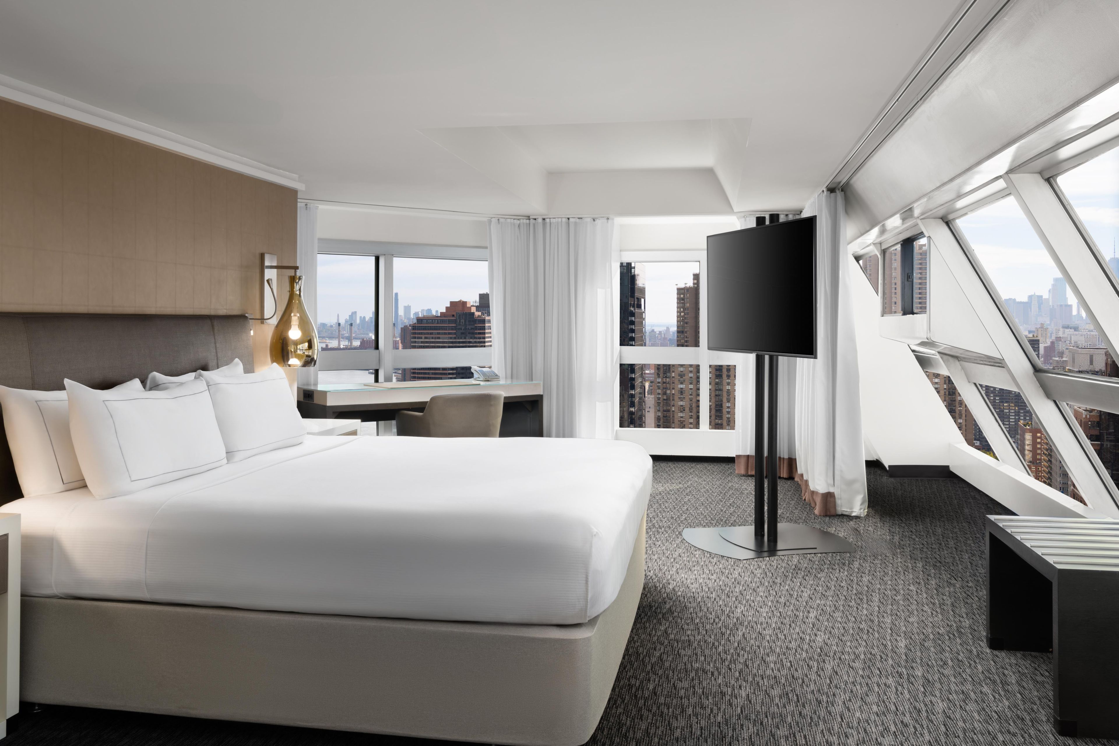 Een hotelkamer met een groot bed, een bureau, een televisie en uitzicht op de stad.