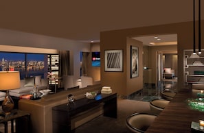 A modern hotel room with a city view, a desk with a lamp, a sofa, and a dining area with chairs.
