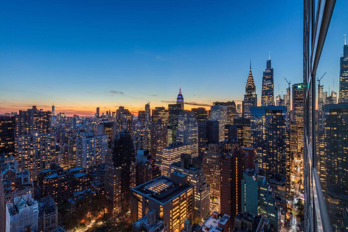 Une vue sur la ville au crépuscule, avec des gratte-ciel illuminés et une vue dégagée sur l’horizon.