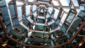 Een geometrische glazen constructie met een centraal honingraatpatroon en omliggende reflecterende oppervlakken.