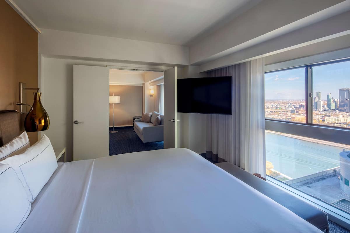 Une chambre d’hôtel avec un grand lit, un téléviseur fixé au mur et une vue sur la ville grâce à une grande fenêtre.