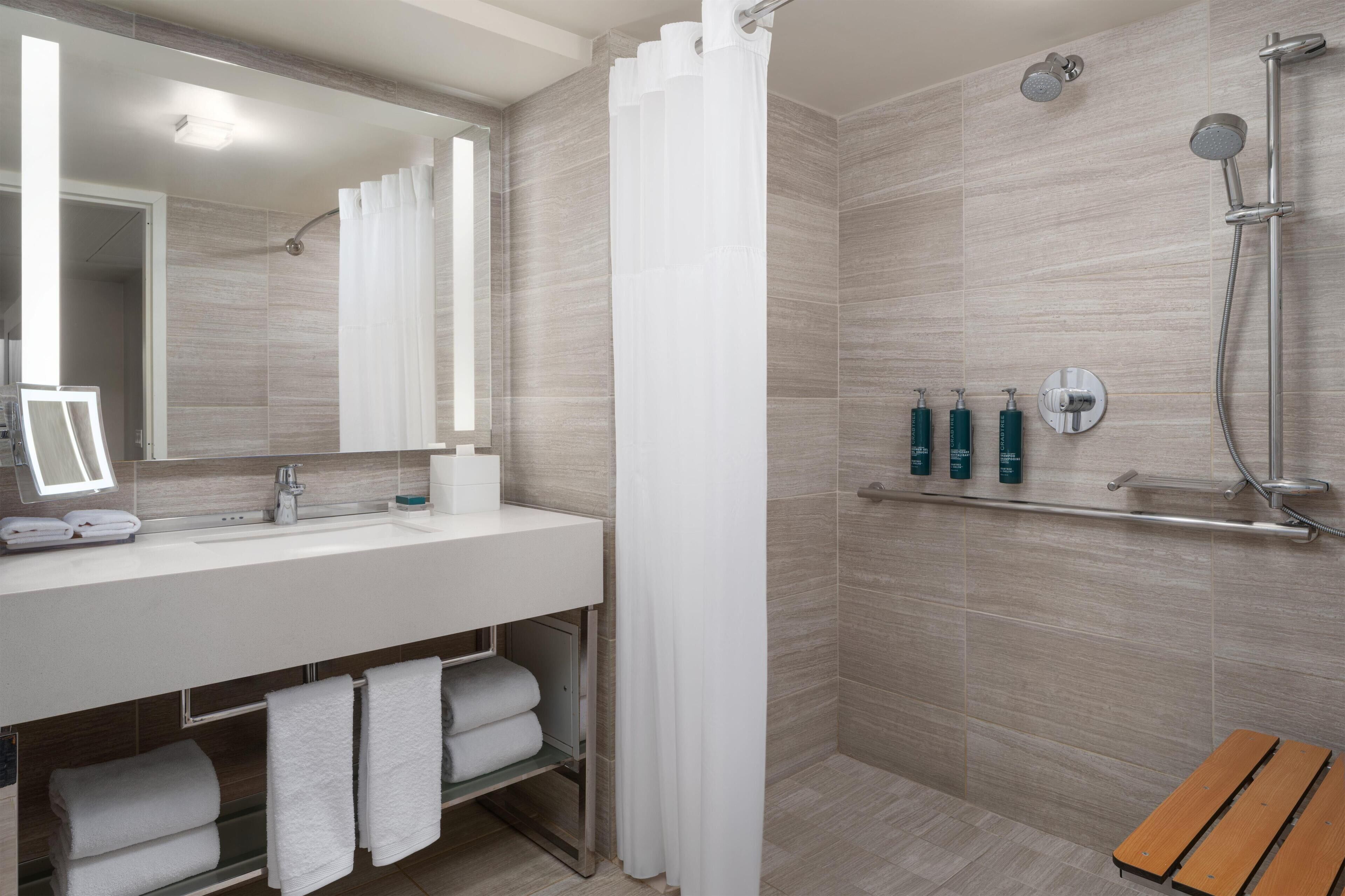 A modern bathroom with a shower, a sink with a mirror, and a bench.
