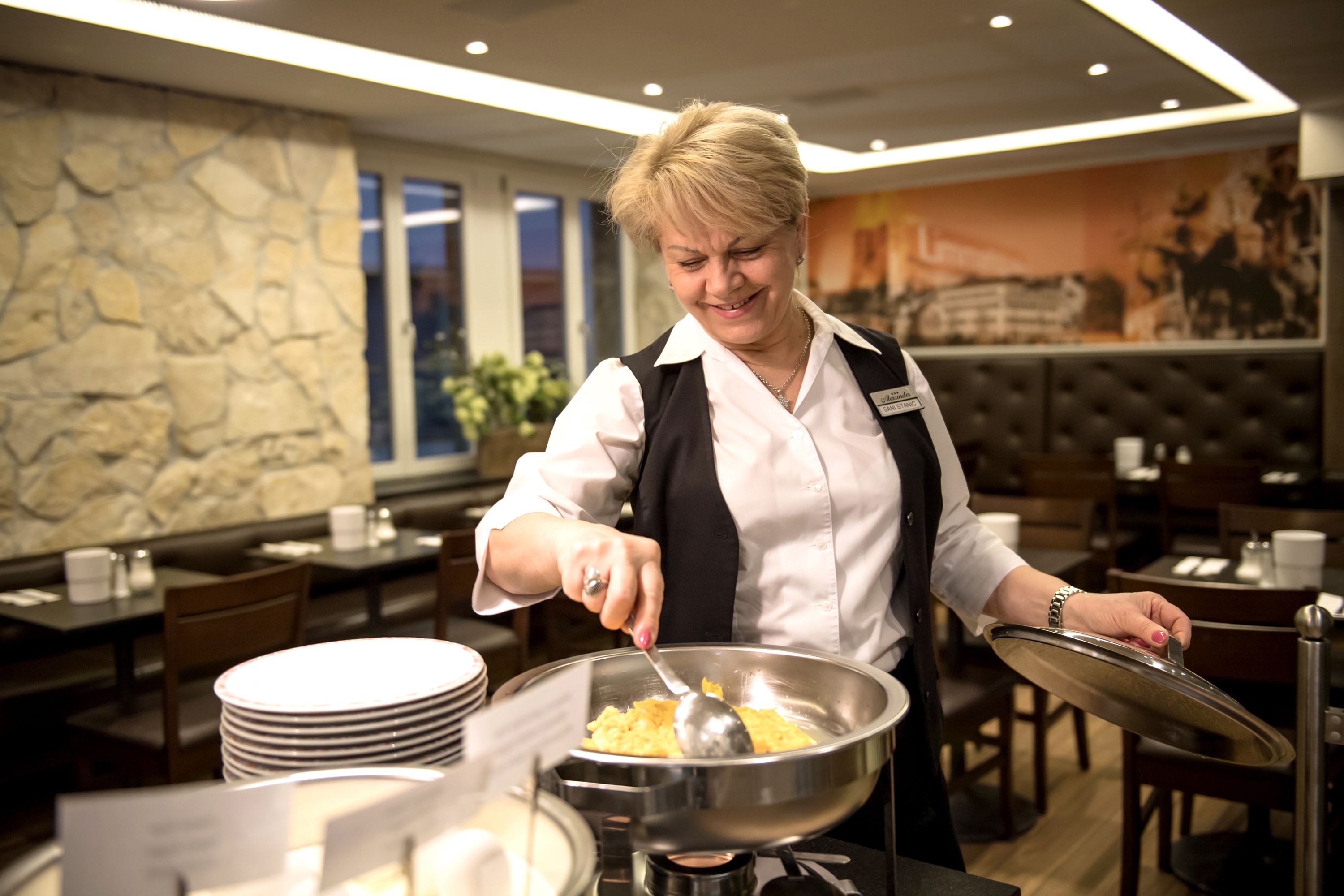 A person cooking in a restaurant with a stone wall and a mural in the background.