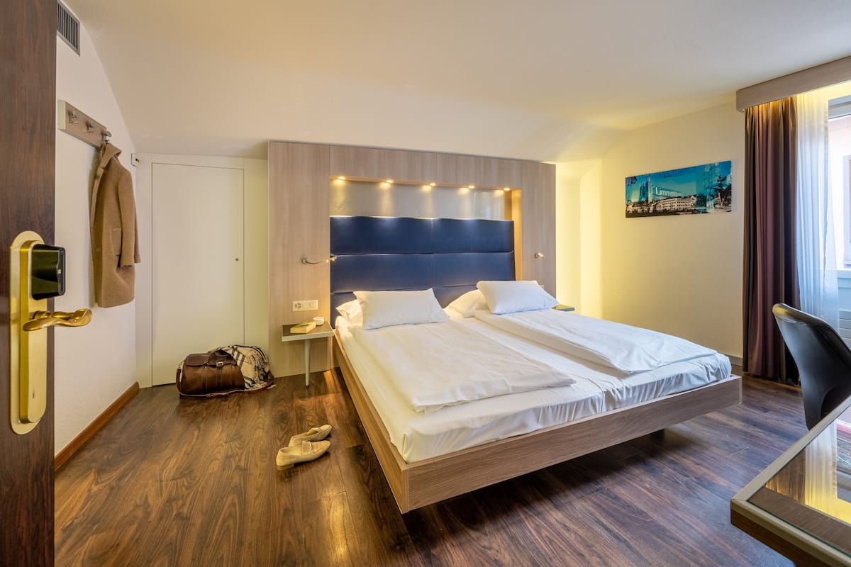 A hotel room with a wooden bed, a nightstand, a coat rack, and a painting on the wall.