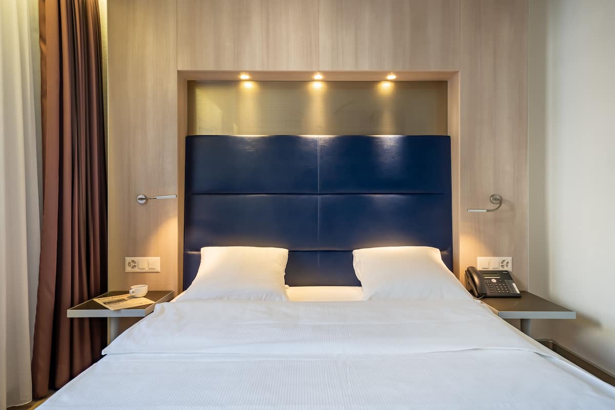 A hotel room with a large bed, a bedside table with a phone, and a tray with a cup and a menu.