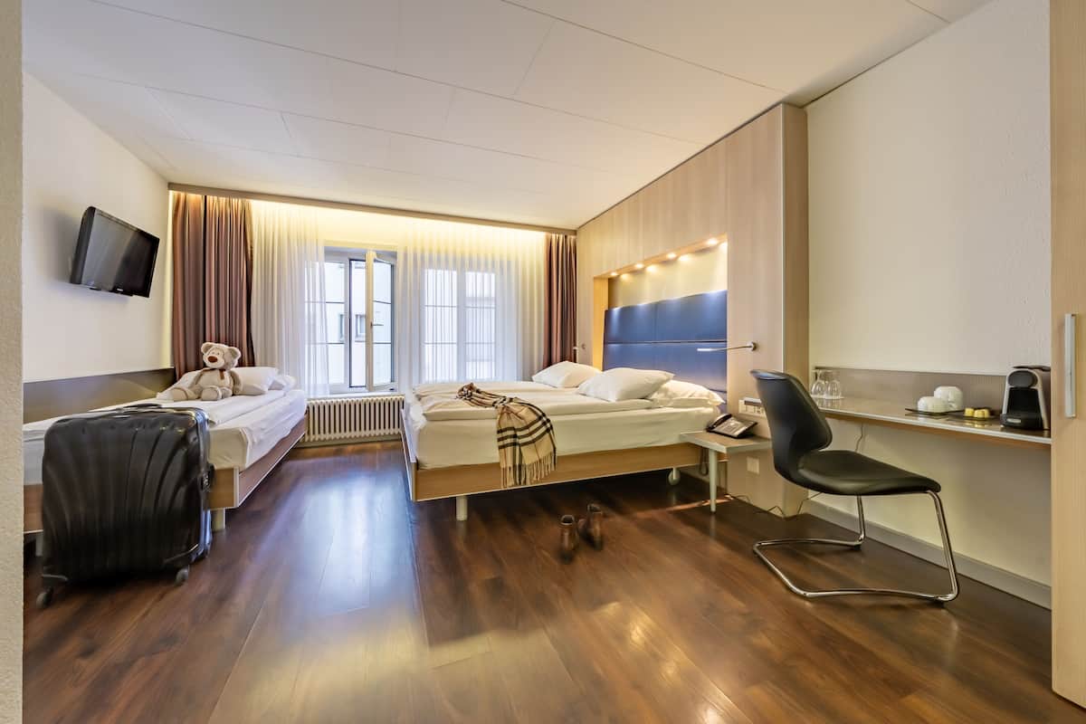A hotel room with a bed, a desk, a chair, a television, and a window with curtains.