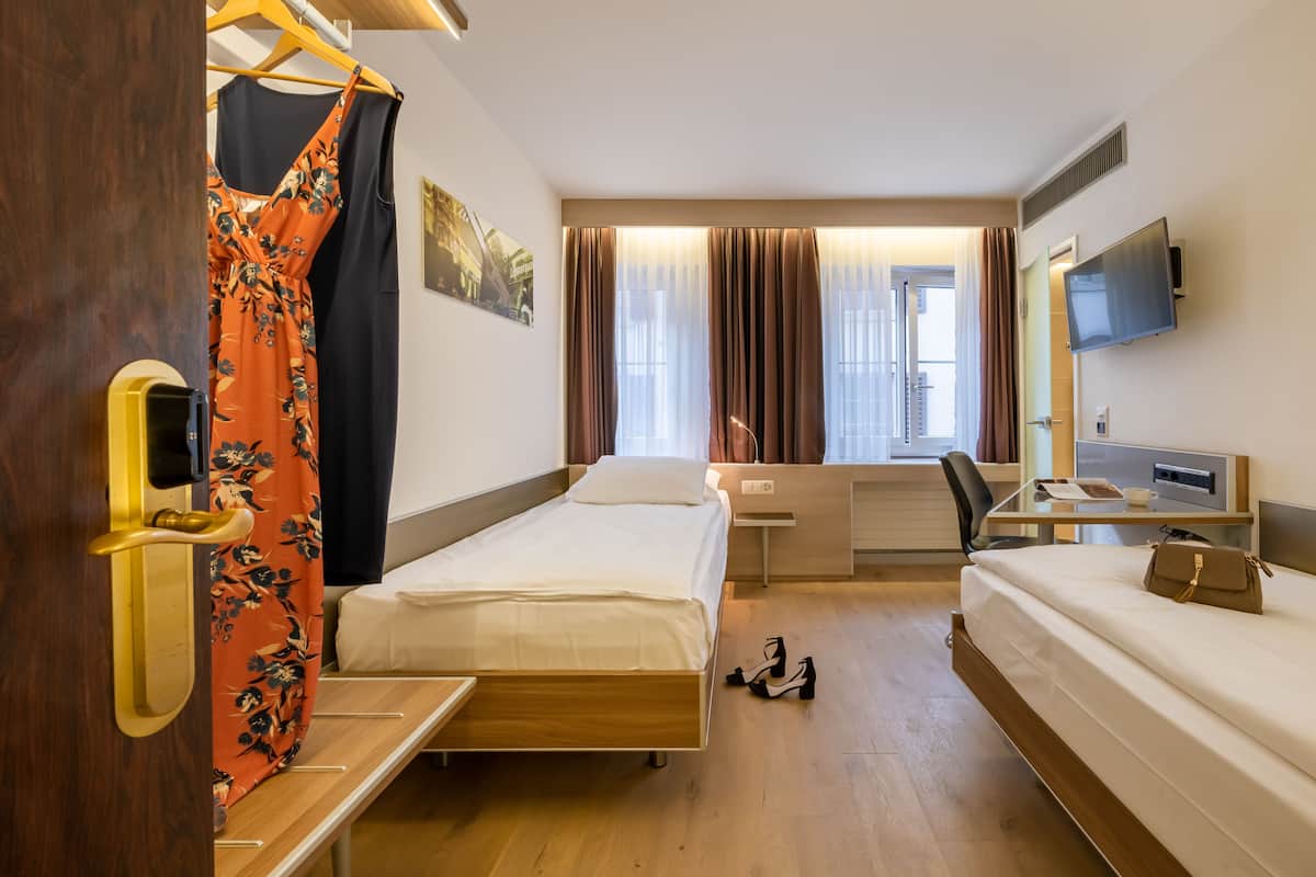 A hotel room with a wooden bed, a desk with a chair, a TV, and a window with curtains.