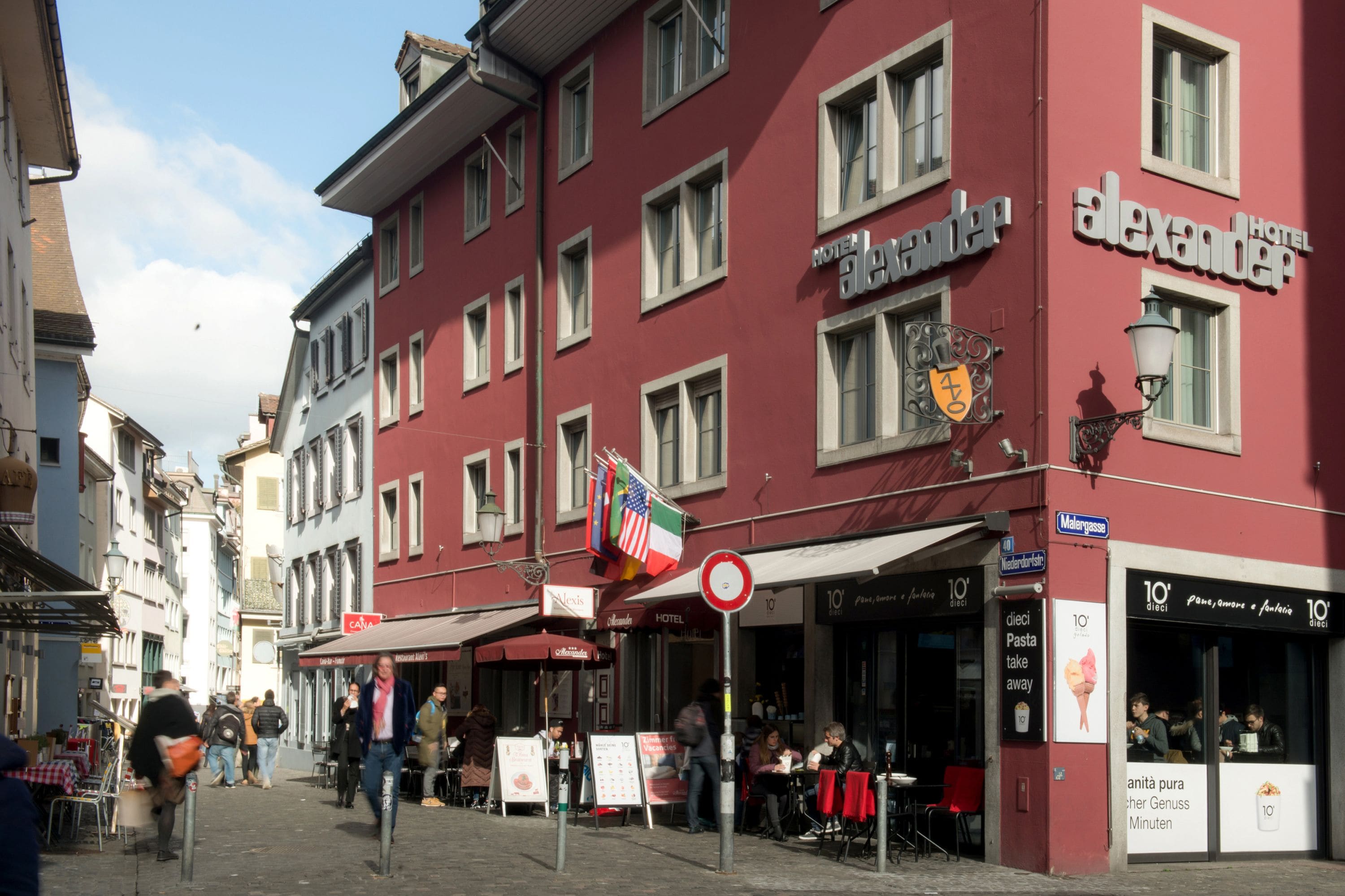 A red building with a sign for 'Hotel Alexander' and a flag display.