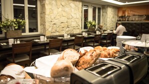 Un bufé de desayuno con panes y bollería variados, una pared de piedra y un comedor con mesas y sillas.
