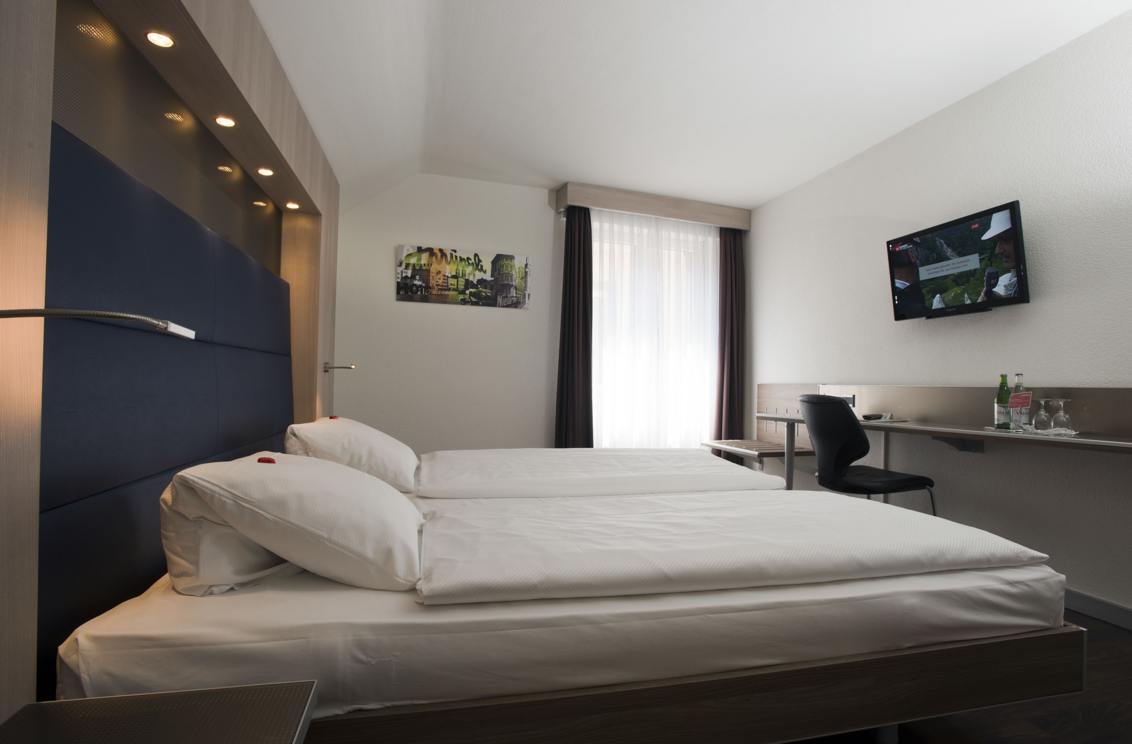 A modern hotel room with a large bed, a desk, and a TV mounted on the wall.