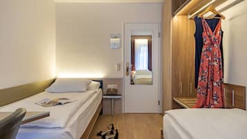 Habitación de hotel con dos camas, una mesita de noche, un espejo, un vestido colgado y un par de zapatos en el suelo.