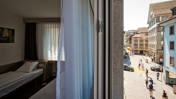 Habitación de hotel con cama, escritorio y ventana con vistas a una calle concurrida.