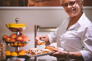A person holding a plate with pastries and a bowl of fruit in the background.