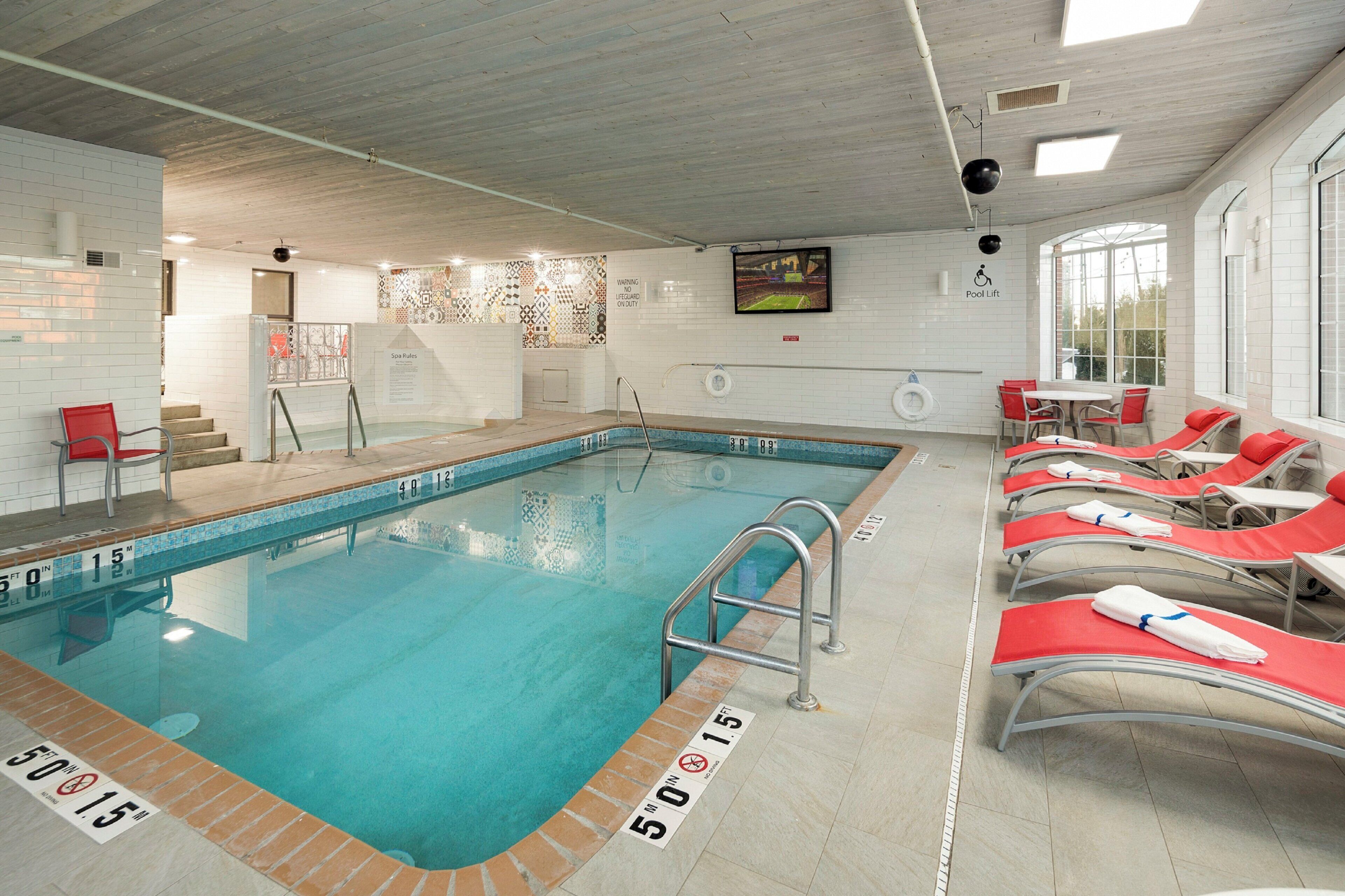 Piscina interna com chão revestido de azulejos, elevador de piscina e espreguiçadeiras com toalhas.