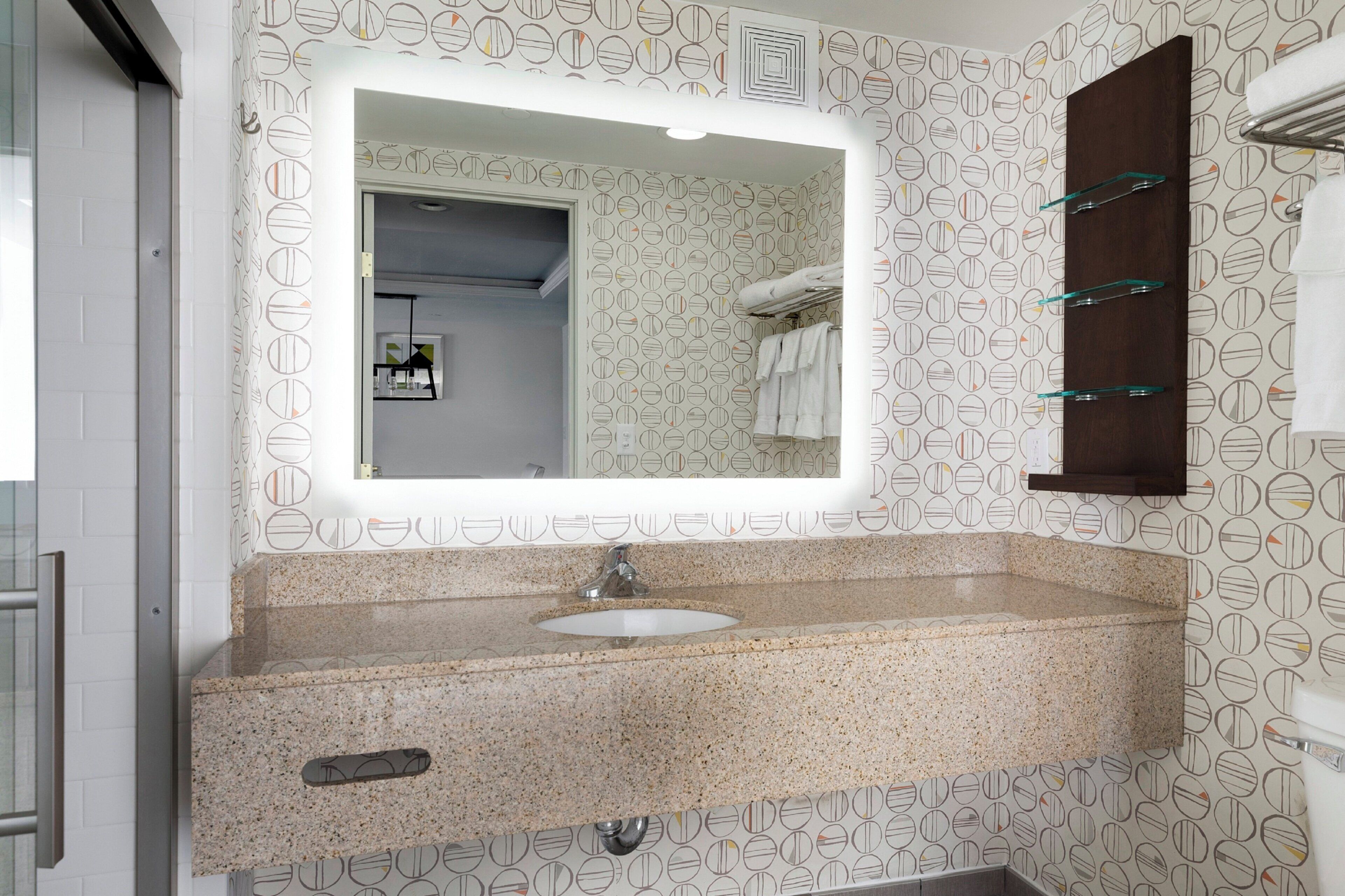 Un baño con encimera de granito, un lavamanos, un espejo y un perchero para toallas.