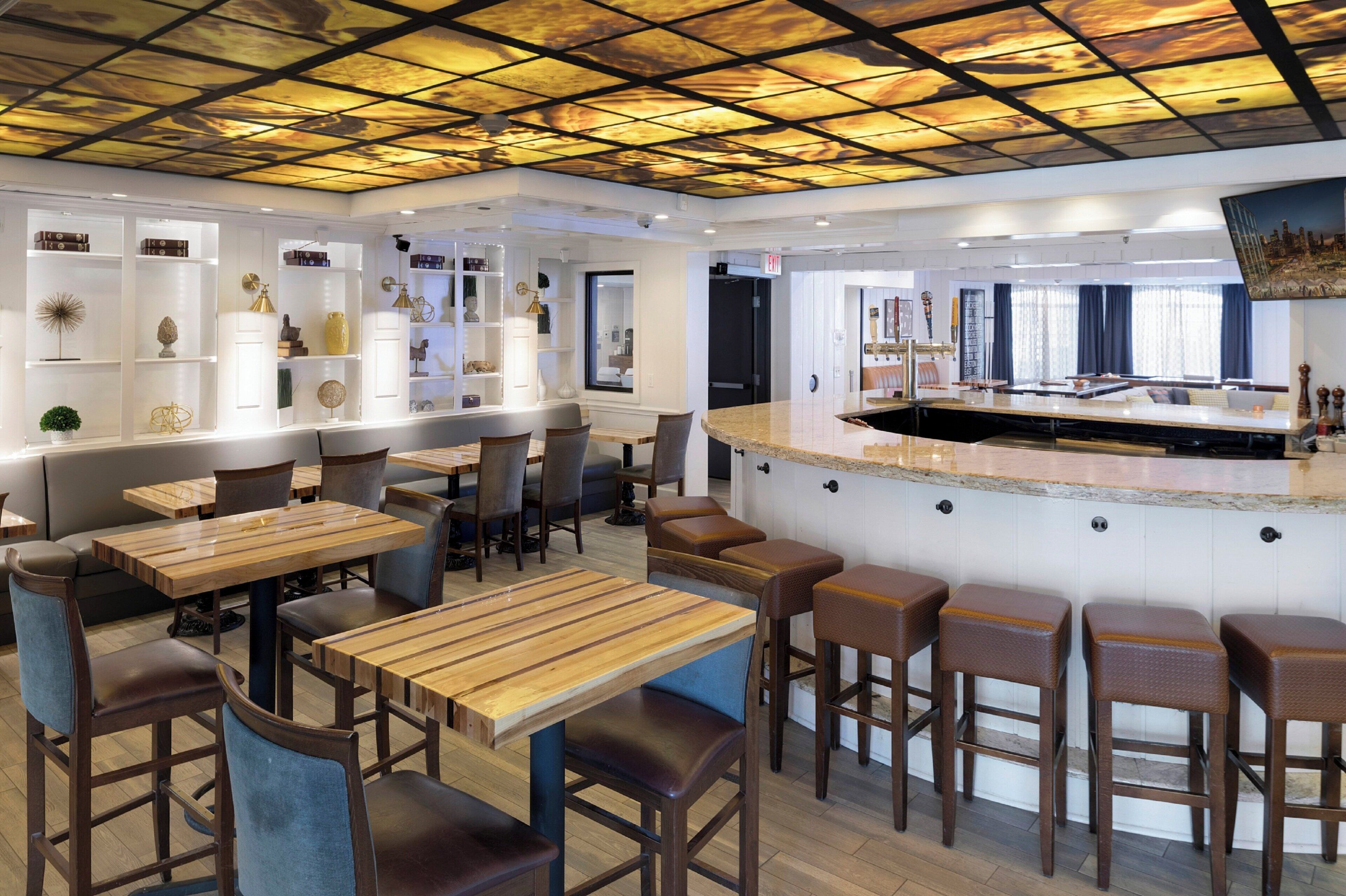 A restaurant interior with wooden tables and chairs, a bar area, and a ceiling with a grid pattern.