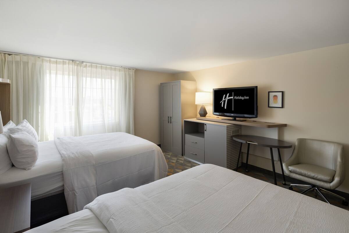 A hotel room with two beds, a desk with a television, a chair, and a cabinet.