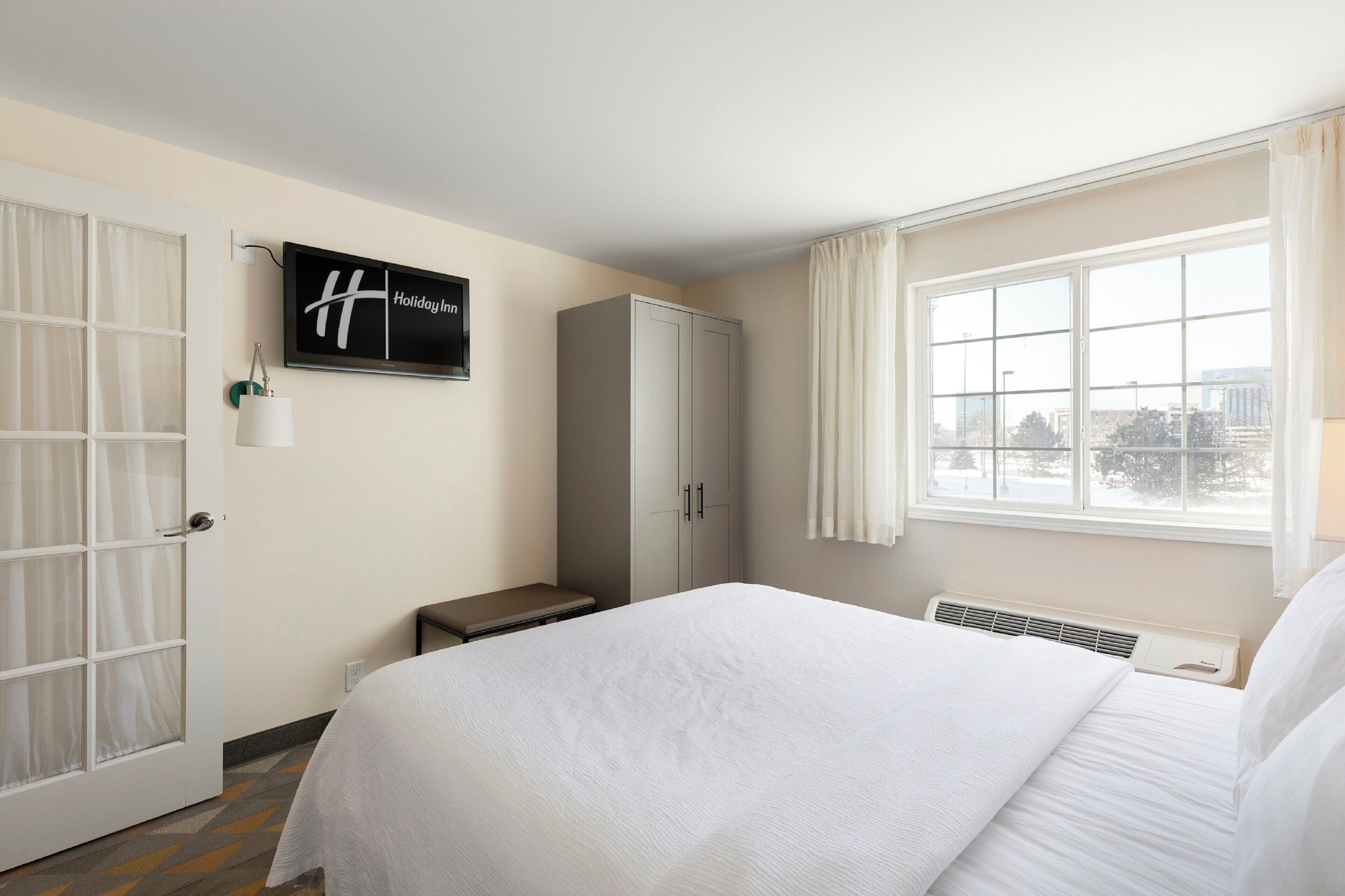A hotel room with a bed, a wardrobe, a desk, a chair, a television, and a window with a view.