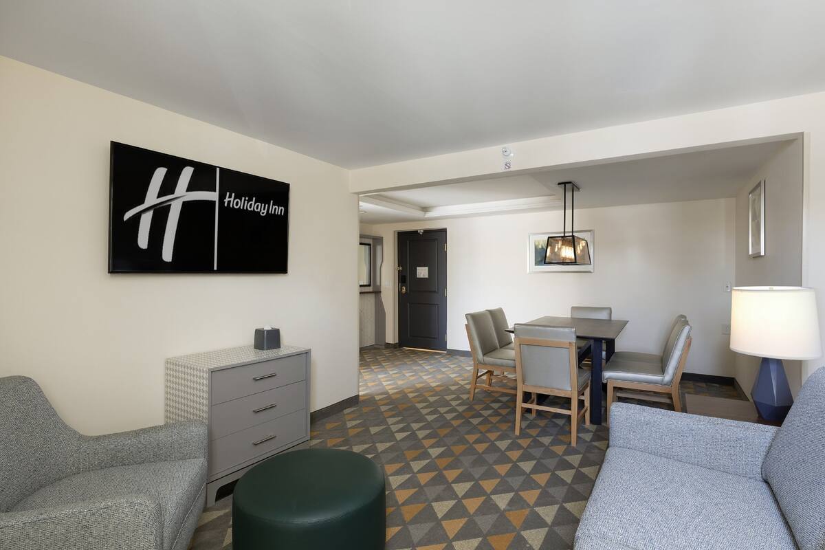 A hotel room with a sofa, a desk, a chair, a lamp, and a wall art piece.