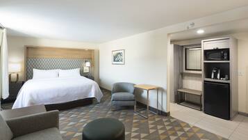 A hotel room with a bed, a small desk, a chair, a sofa, a bench, and a kitchenette.