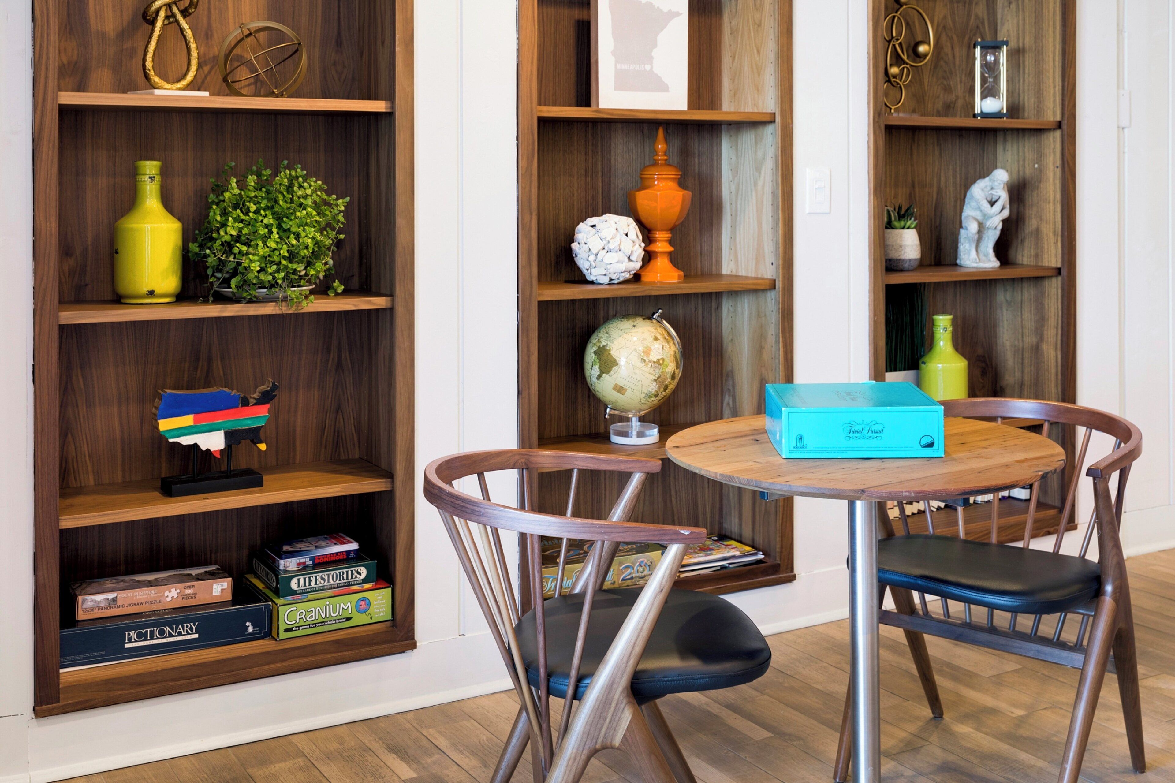 Een kamer met houten planken met boeken, een wereldbol en decoratieve objecten. Er staat een rond tafel met stoelen en een blauwe doos erop.