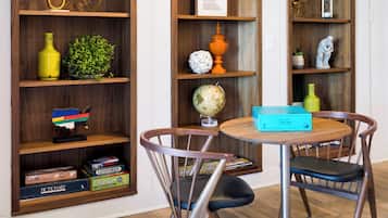 Een kamer met houten planken met boeken, een wereldbol en decoratieve objecten. Er staat een rond tafel met stoelen en een blauwe doos erop.