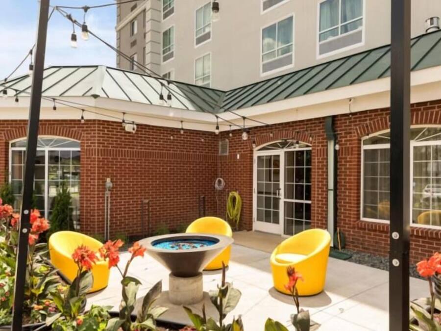 A courtyard with a pool table, yellow chairs, and a brick building with large windows.