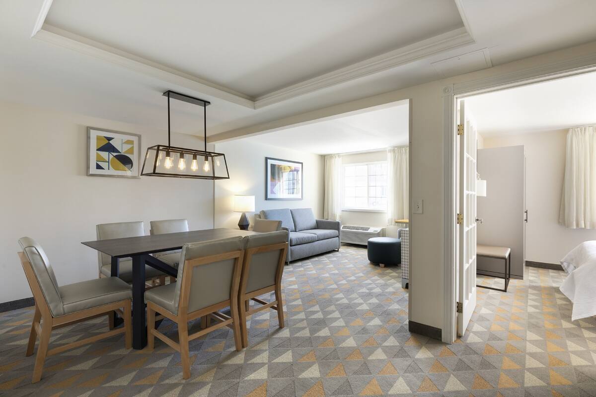 A hotel room with a dining area, a sofa, a bench, and a bed.