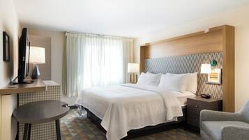 A hotel room with a bed, bedside table, chair, desk, and a television.