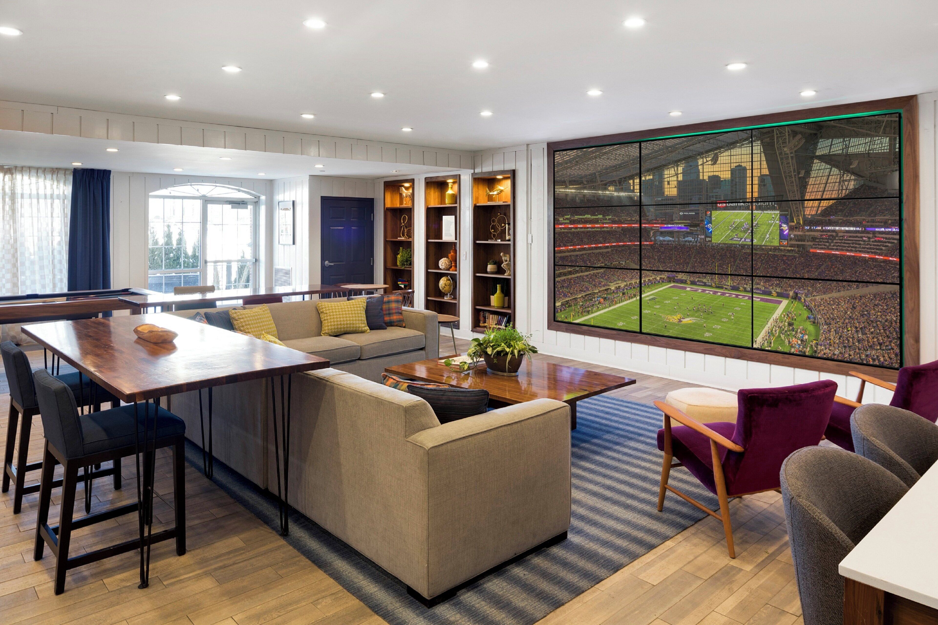 Uma sala de estar moderna com uma televisão grande exibindo um evento esportivo, uma área de refeições com mesa de madeira e um canto de estar aconchegante.