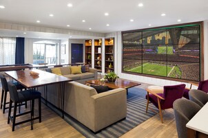 Una sala moderna con un televisor grande mostrando un evento deportivo, un comedor con una mesa de madera y una zona de estar acogedora.