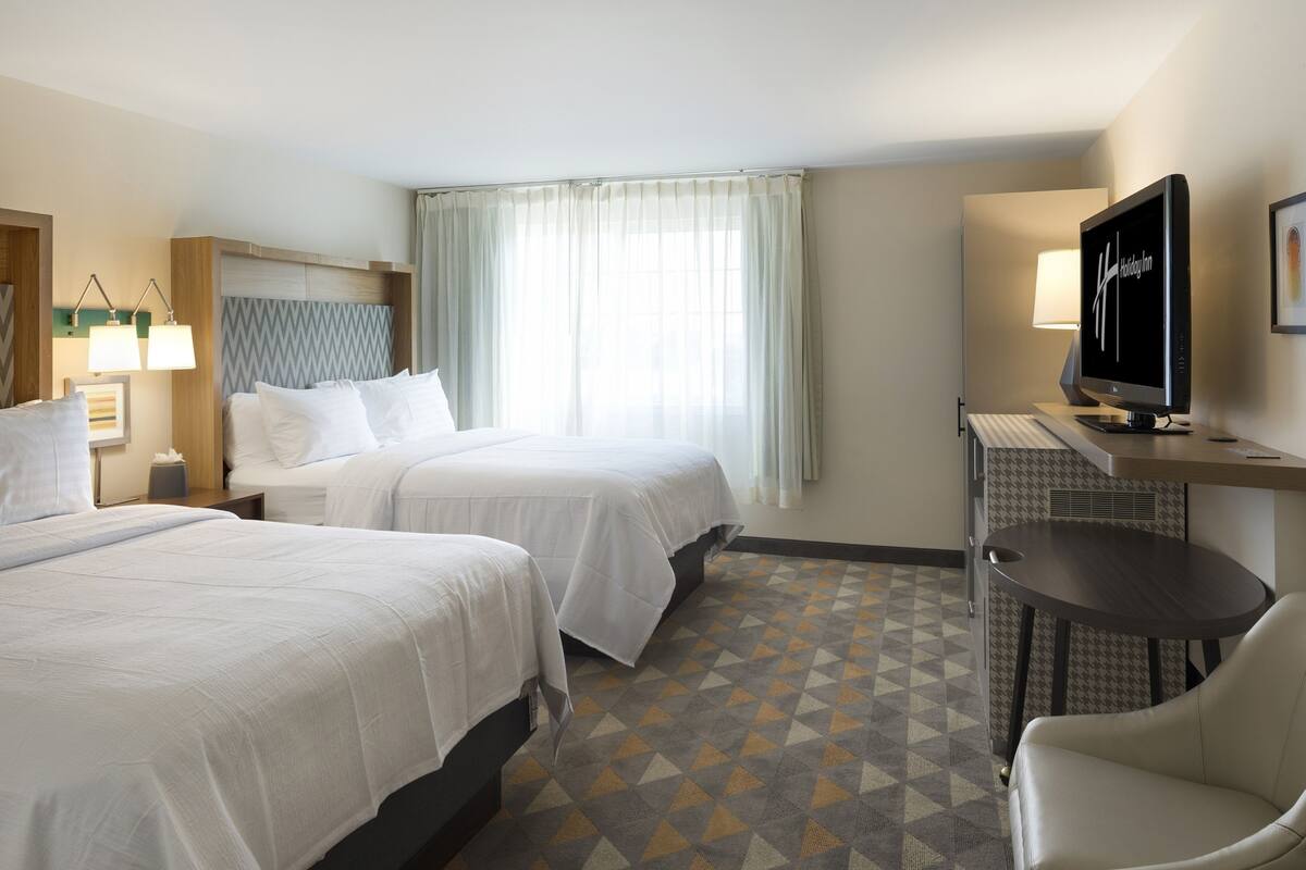 A hotel room with two beds, a desk with a computer, a chair, and a TV.