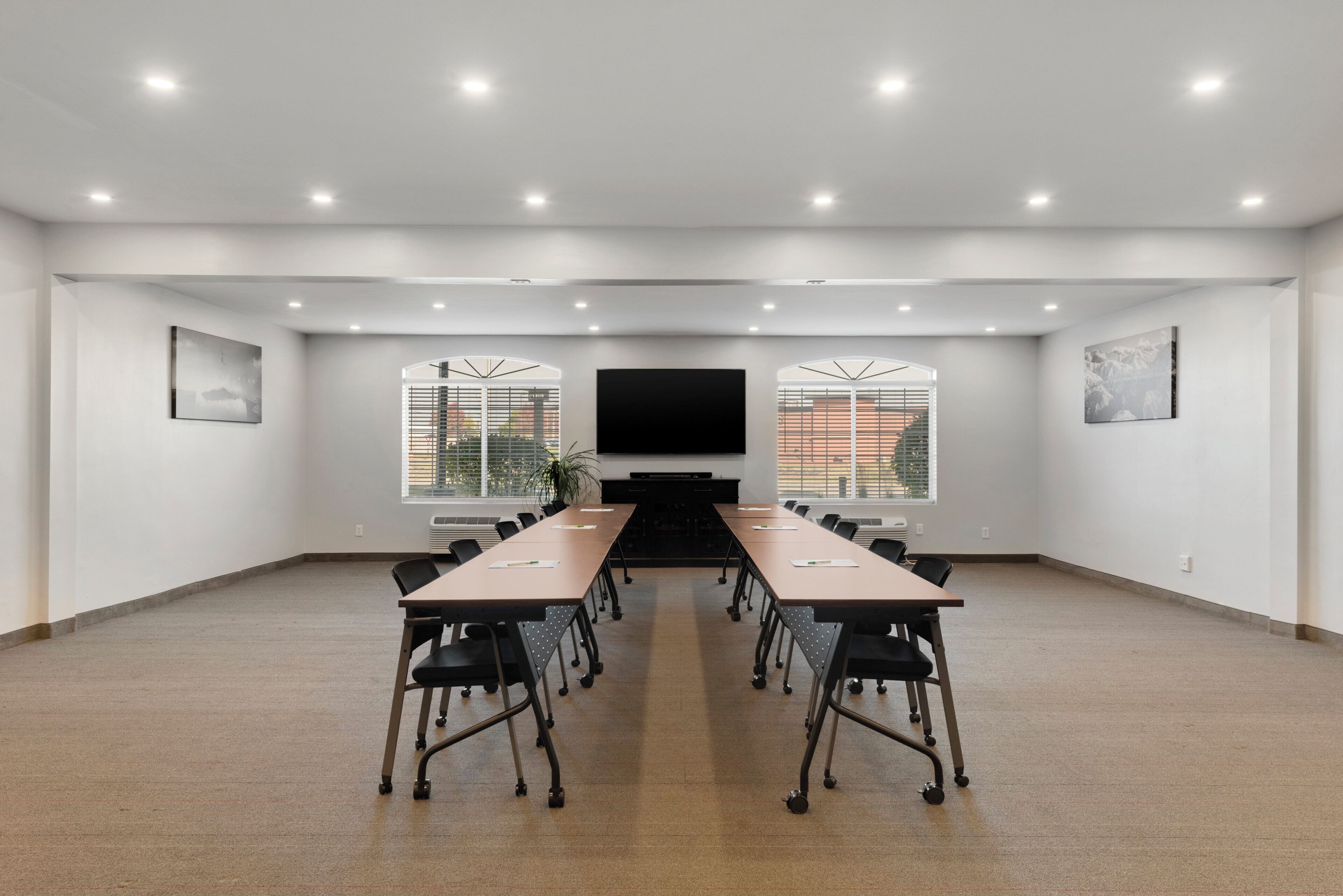 A conference room with a long table, chairs, a flat-screen TV, and windows with blinds.