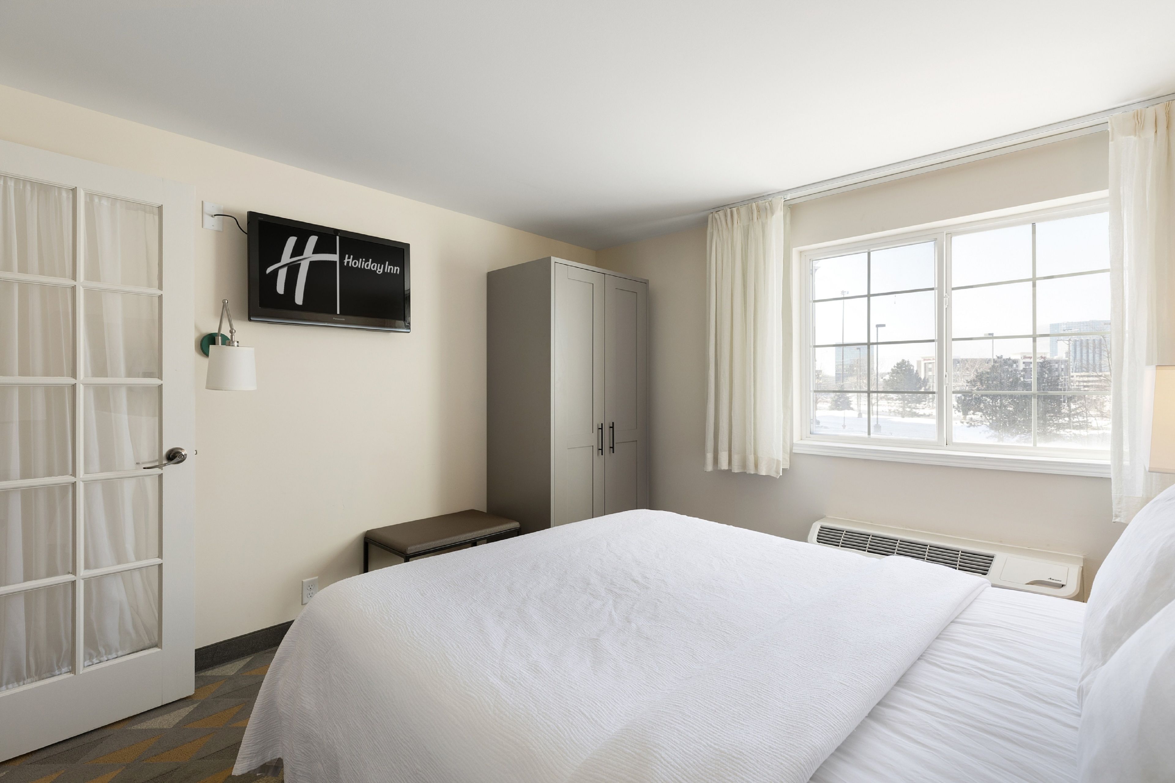 A hotel room with a bed, a wardrobe, a bench, a TV, and a window with a view.