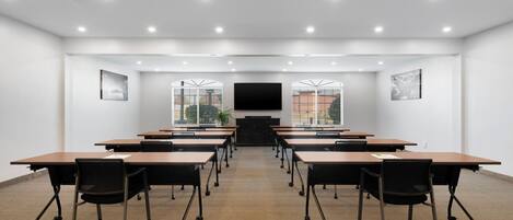 A conference room with a long table, chairs, a flat-screen TV, and windows with blinds.