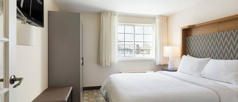 Una habitación de hotel con una cama, un banco, una ventana con cortinas, un televisor en la pared y un piso con diseño.