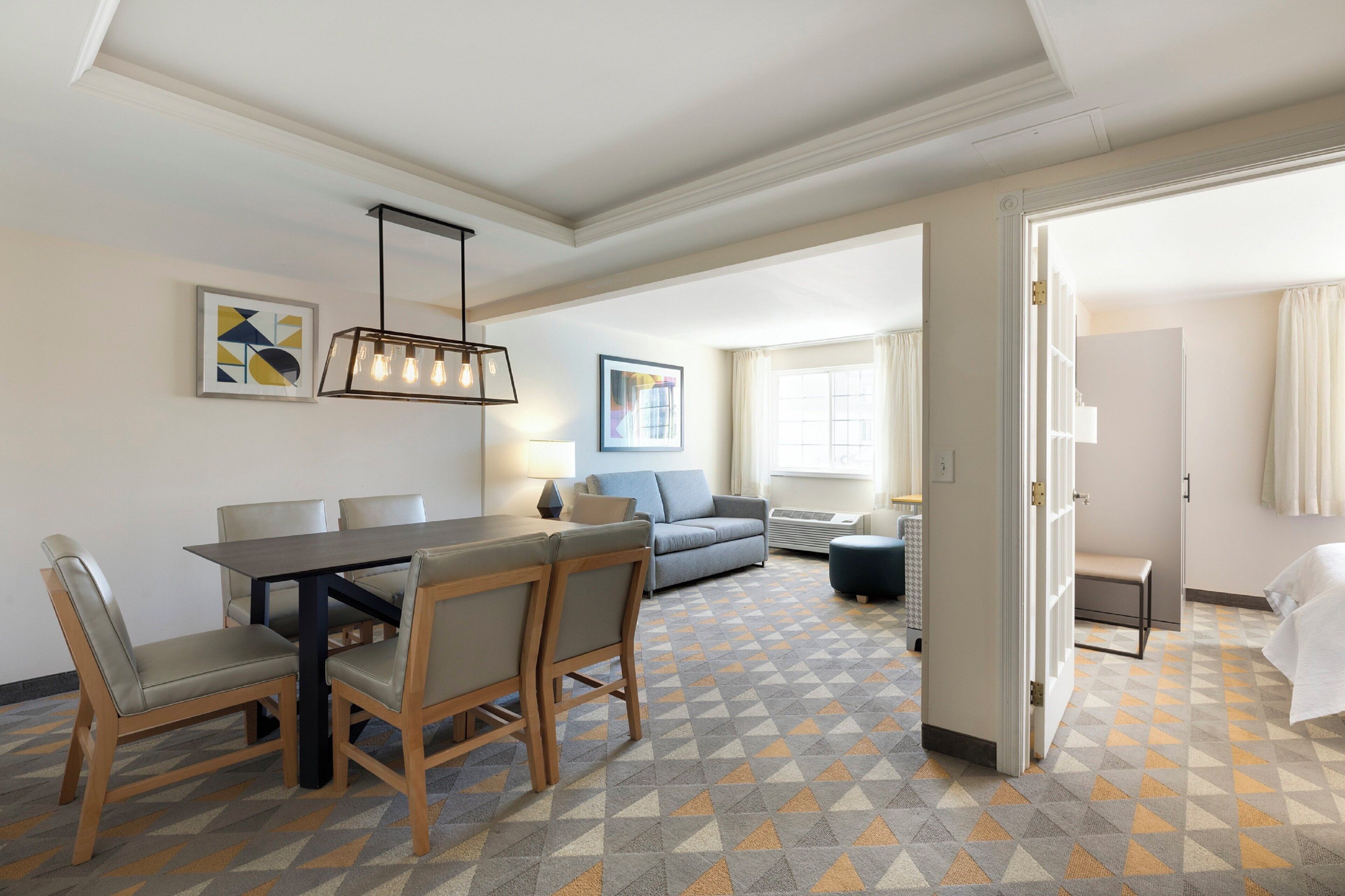 A hotel room with a dining area, a sofa, and a view of the outside.
