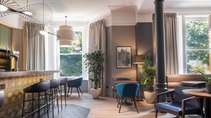 Un espace bar moderne avec des tabourets, un comptoir et des luminaires suspendus. Des plantes en pot et un canapé agrémentent un coin salon confortable.
