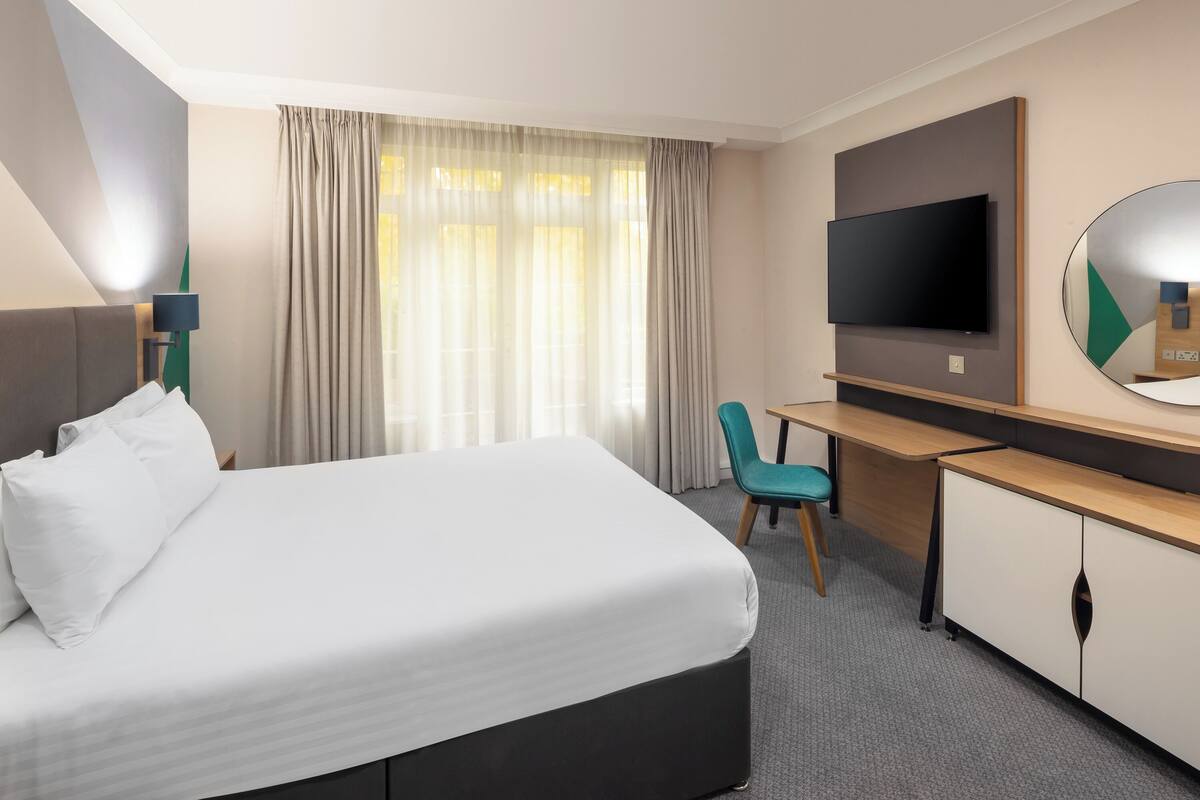 Ein Hotelzimmer mit Bett, Schreibtisch, Stuhl, Fernseher und Spiegel.