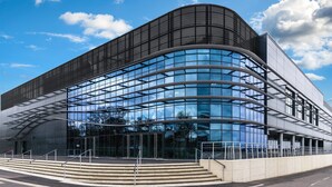Un bâtiment moderne doté d’une façade en verre incurvé, de grandes fenêtres et d’un toit plat.