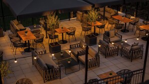 Un espace extérieur aménagé en terrasse, avec plusieurs tables et chaises, protégé par de grands parasols et illuminé de guirlandes lumineuses.