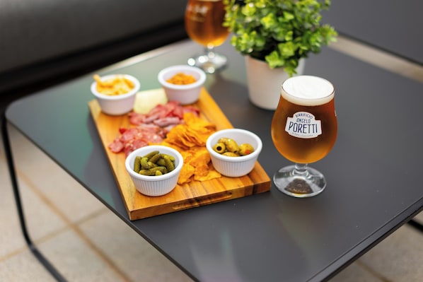 A wooden board with various cheeses, meats, and olives, accompanied by a glass of beer on a table.