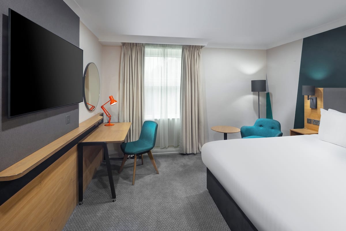 Ein Hotelzimmer mit Bett, Schreibtisch, Stuhl, Fernseher und einem Fenster mit Vorhängen.