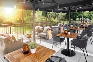 An outdoor patio area with tables and chairs, surrounded by a railing, and overlooking a garden.