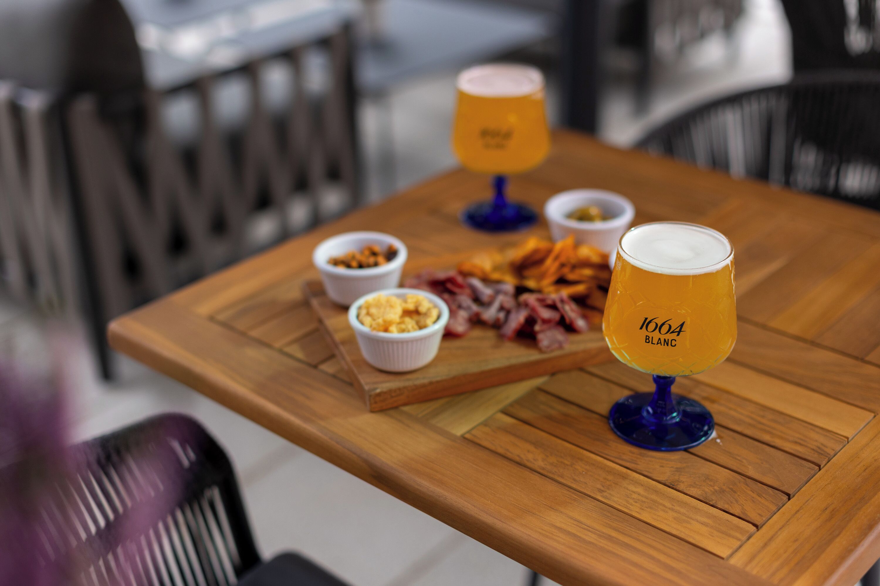 Une table en bois avec un verre de bière, un bol de noix et une assiette de nourriture.