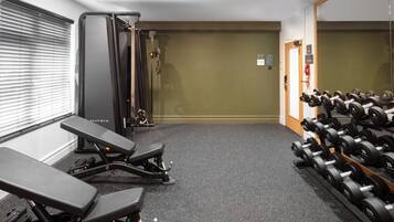Uma academia com equipamentos de exercícios, um banco e uma barra com halteres.